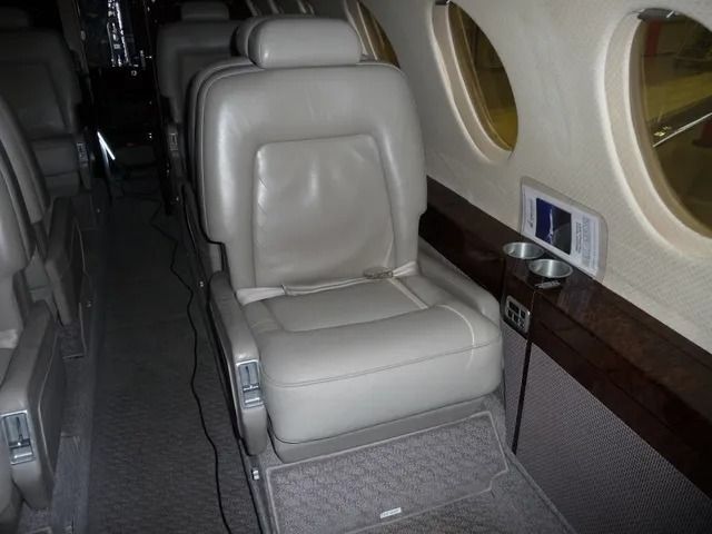 Empty luxury airplane seat by round window, with gray leather seat and dark carpeted floor.