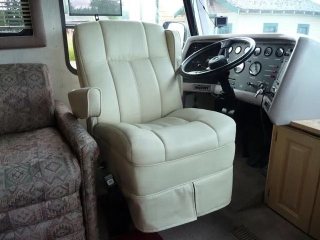 Cream recliner in a RV cockpit with steering wheel and dashboard visible beside patterned sofa.