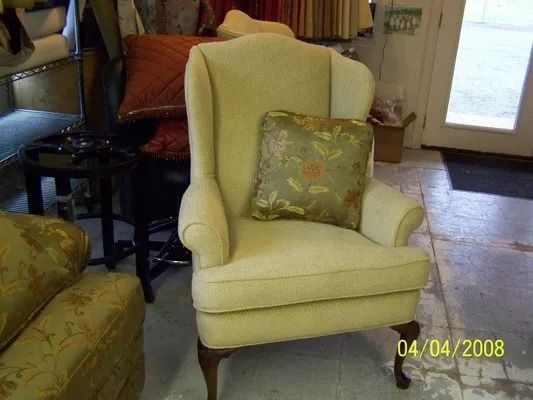 Cream wingback chair with floral pillow in a cozy living room near a window and door.