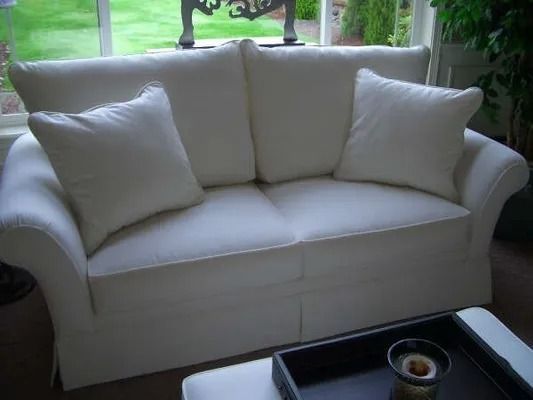 White loveseat with two cushions by a window, with a black coffee table in front.