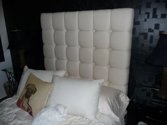 White upholstered headboard above a bed with white pillows in a dark bedroom