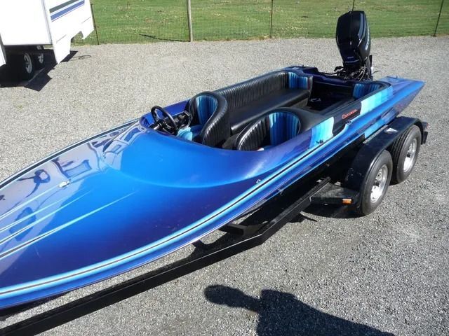 Blue speedboat on a trailer, viewed from the side on a paved lot.