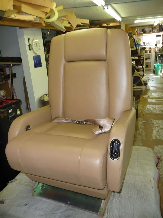 Tan leather recliner chair in a workshop, partially disassembled with exposed components.