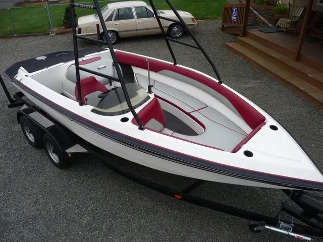 White and red speedboat on a trailer in a driveway, with a car in the background