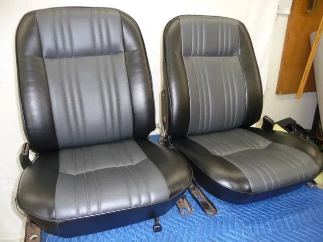 Two black and gray car seats on a blue tarp, with seat belts beside them