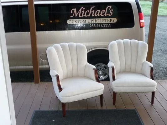 Two white upholstered chairs on a wooden deck beside a black van labeled Michaels