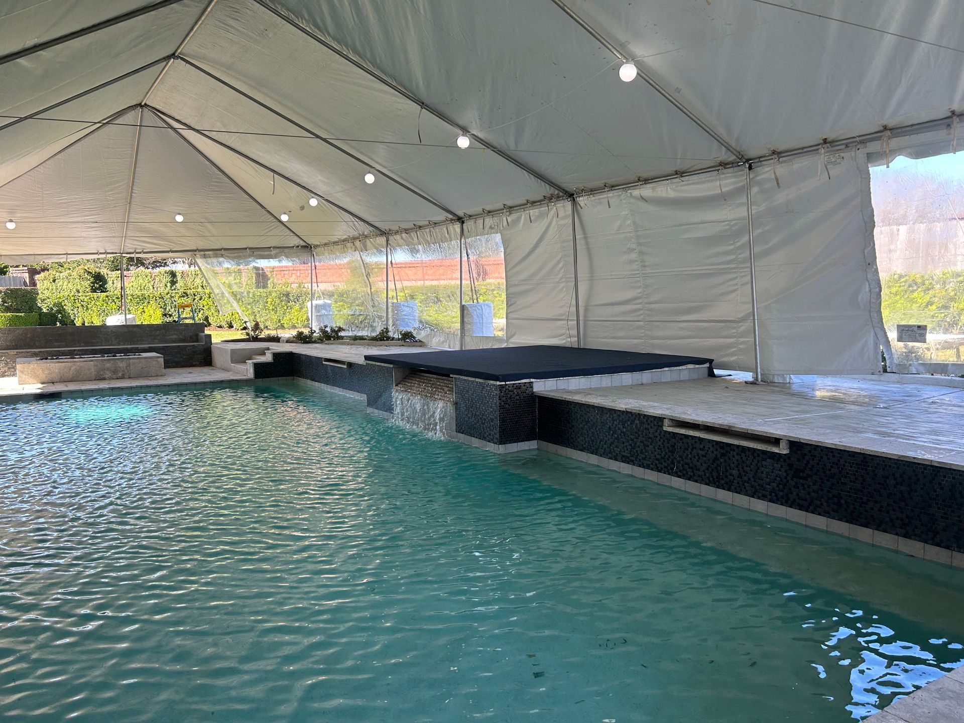 Swimming pool under a white tent, cascading waterfall, and dark tile detailing.
