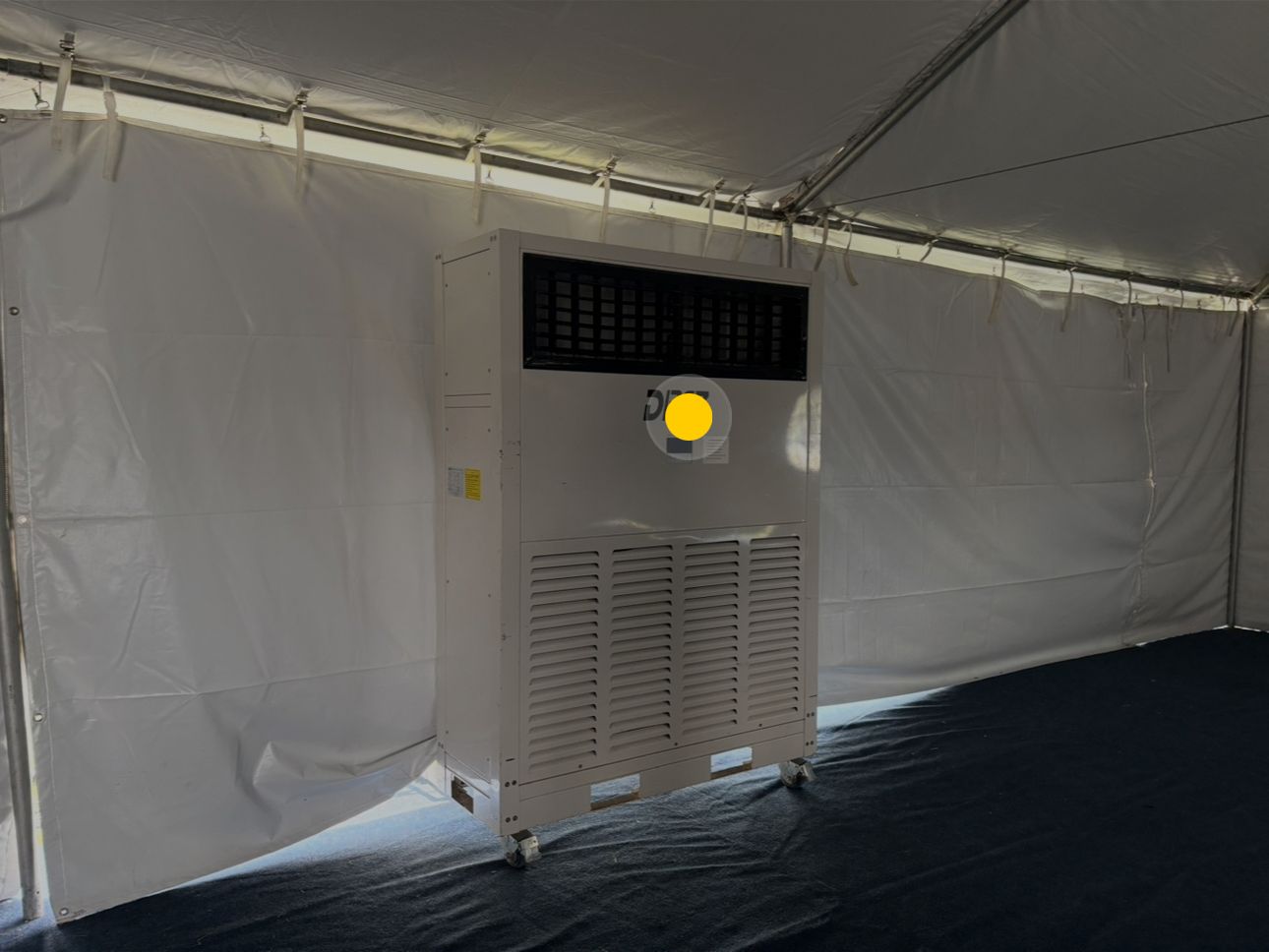 A large, white industrial air conditioner inside a tent with white walls and a dark floor.