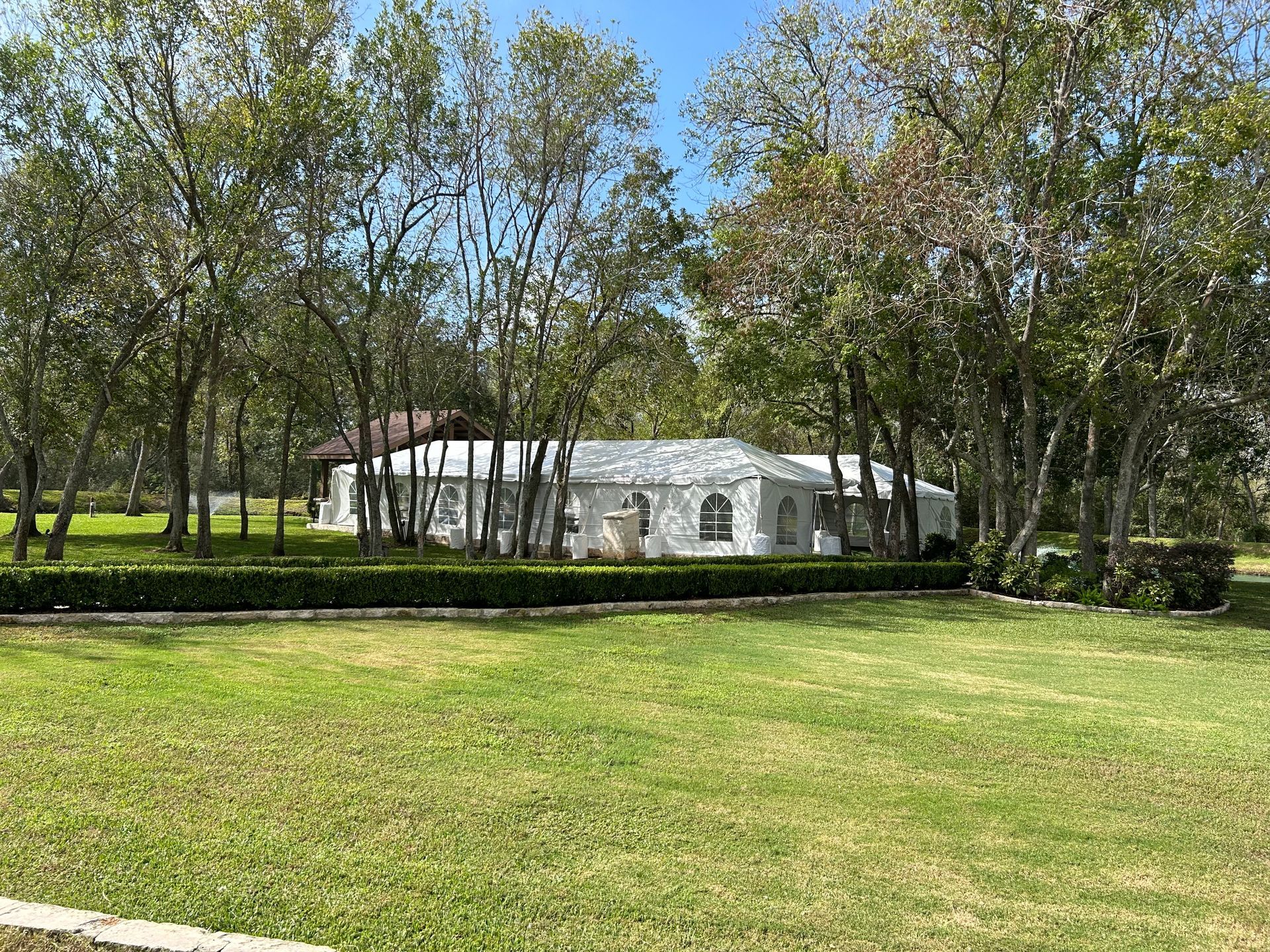 A white stucco building sits behind a green lawn and trees under a bright blue sky.
