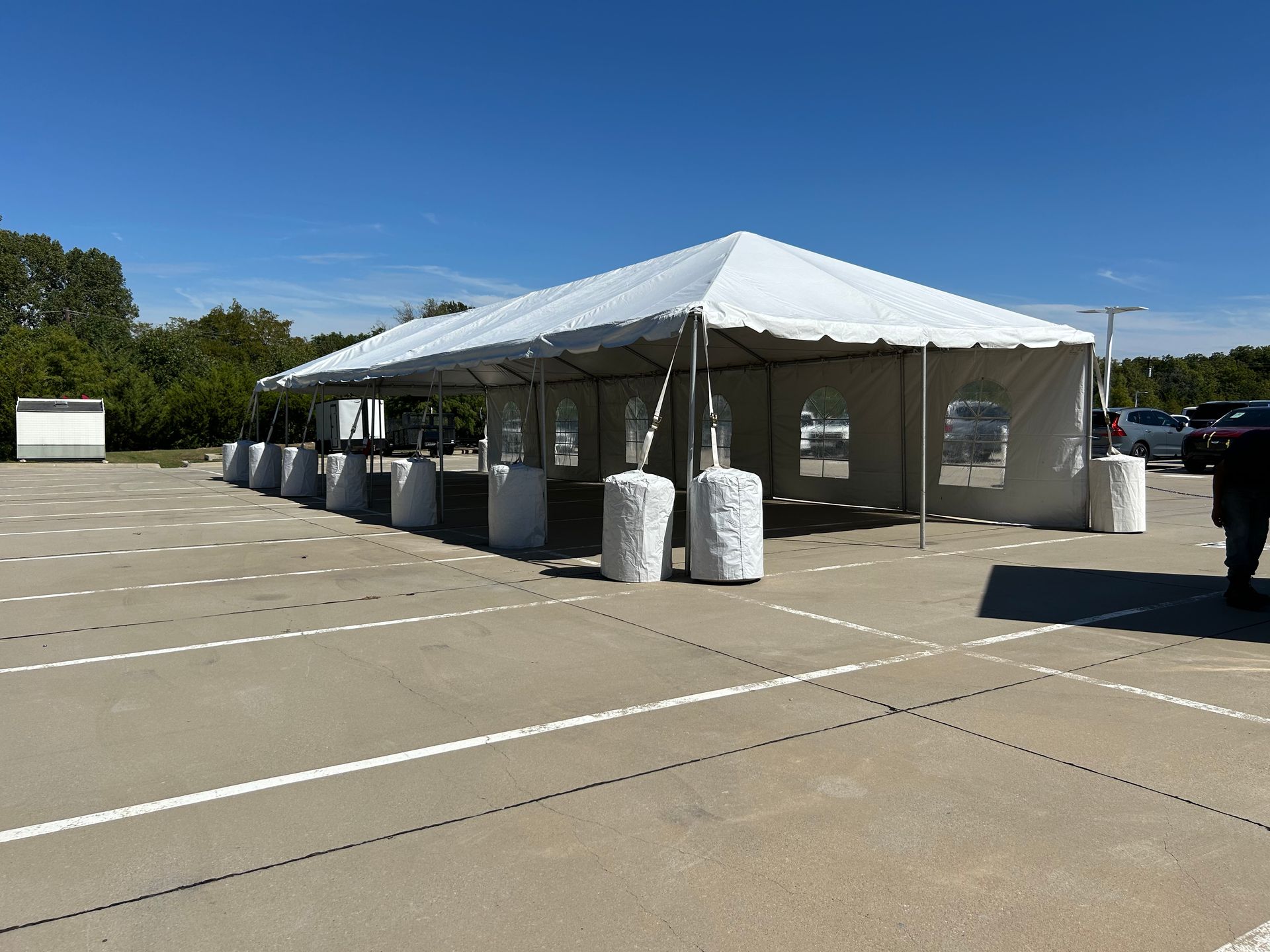 A large white tent set up in a parking lot, likely for an outdoor event. Concrete blocks secure the tent supports.