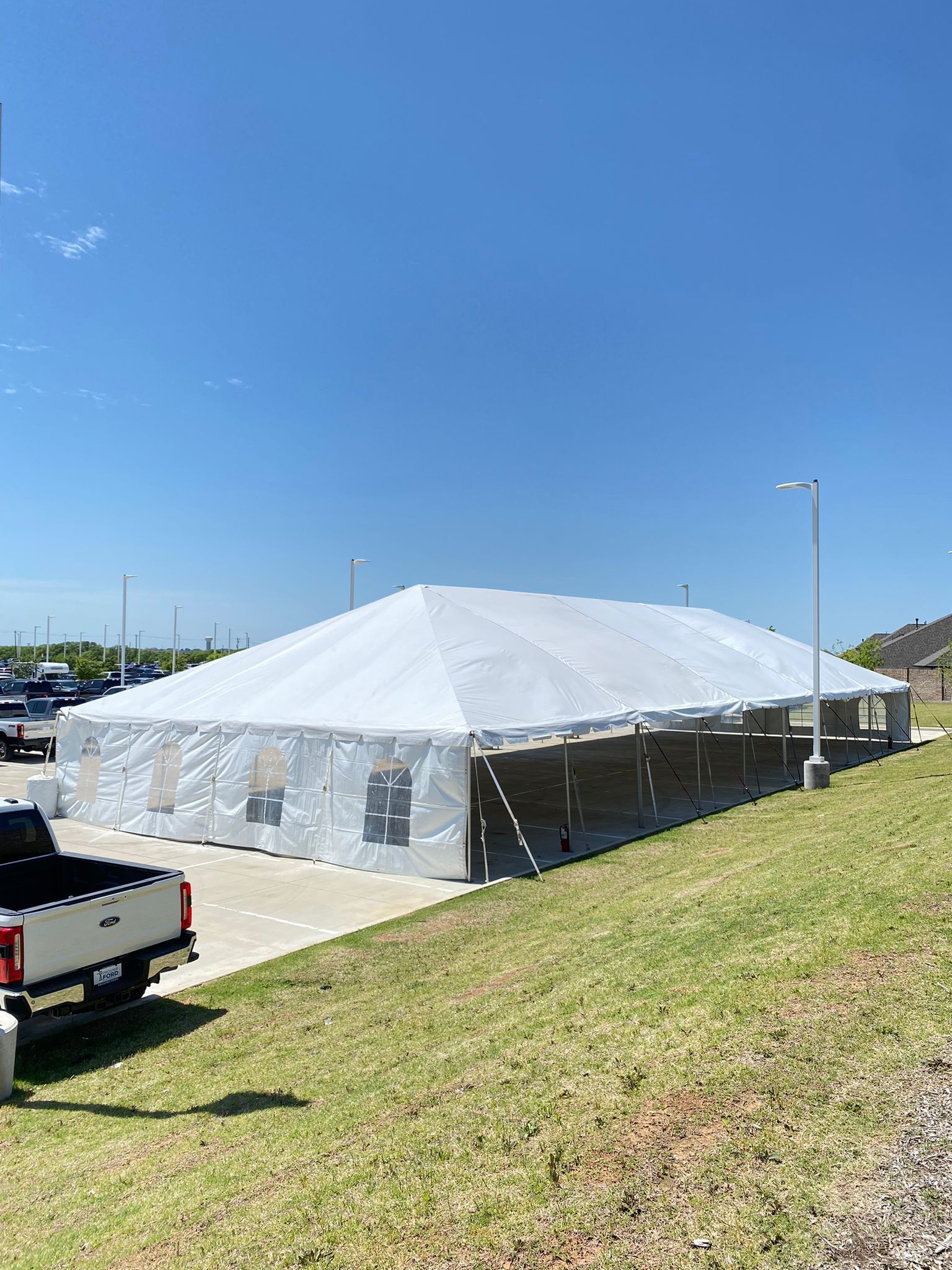 Large white tent on a concrete pad, with a truck in front and a grassy hill. Bright blue sky.