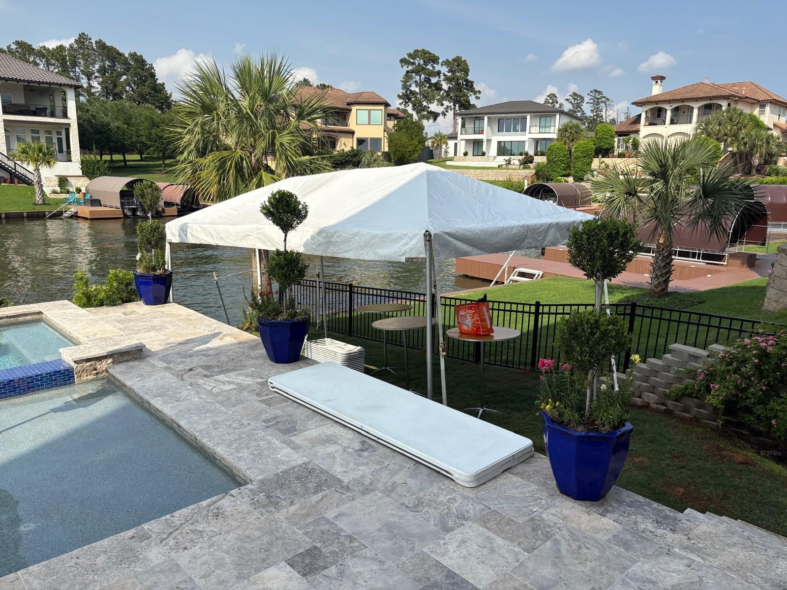 A white tent set up on a patio overlooking a lake, with a pool and houses visible.