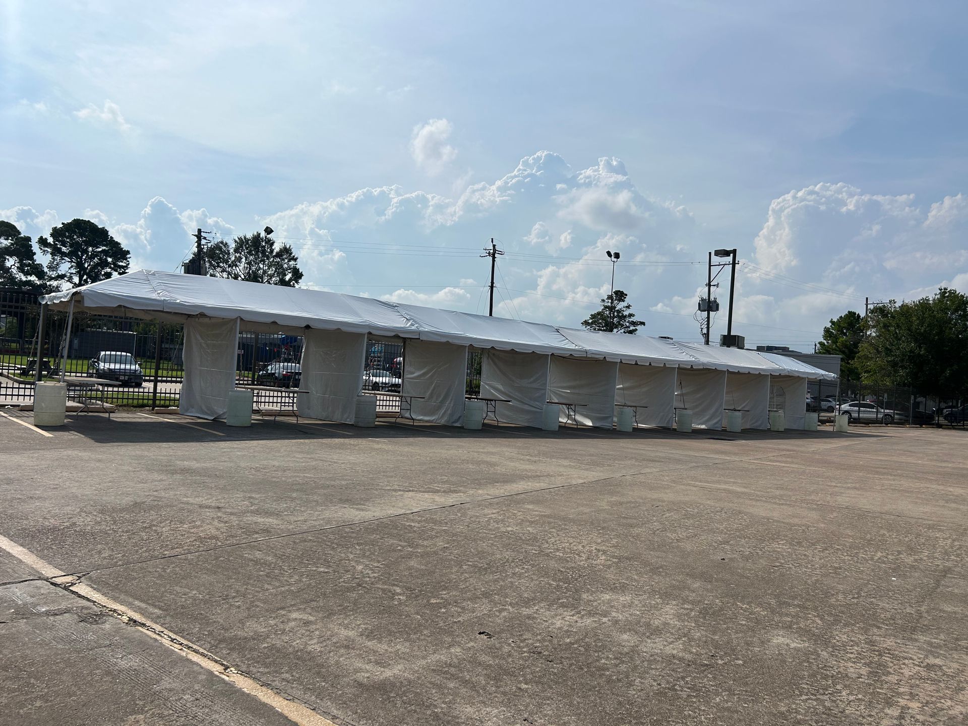 Long, open-air bus shelter with a white roof and columns. The structure is in a parking lot with a cloudy sky overhead.