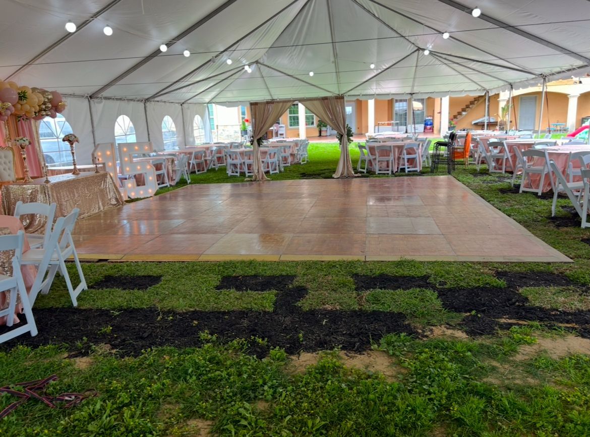 Tent with wooden dance floor, tables, and chairs set up on a lawn for an event.
