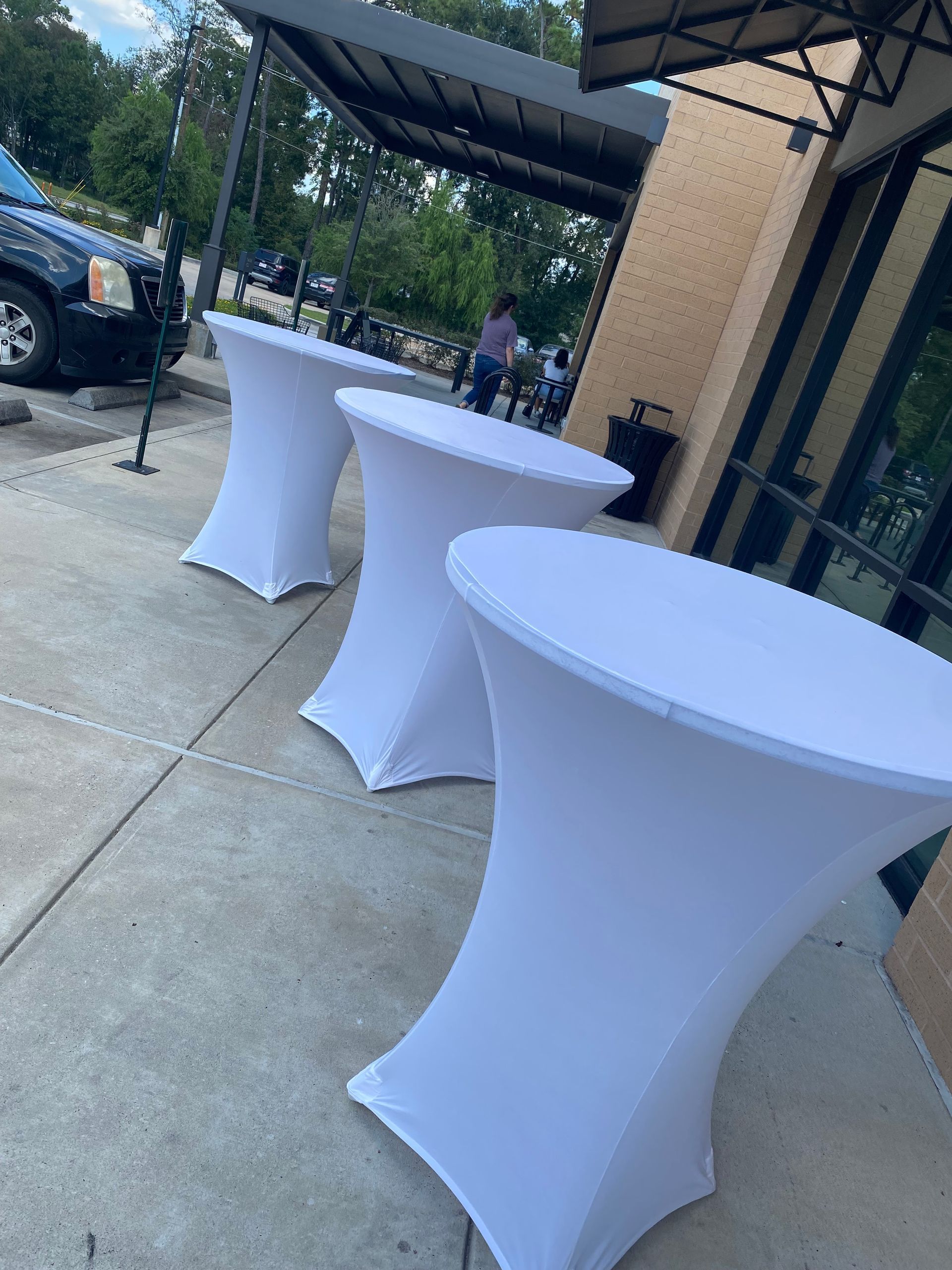 Three white cocktail tables set outside a building on a concrete walkway.