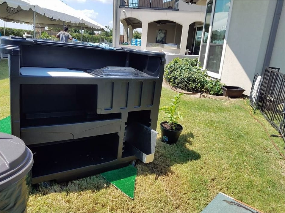 Black outdoor bar with a white countertop, set on green grass in front of a large house.
