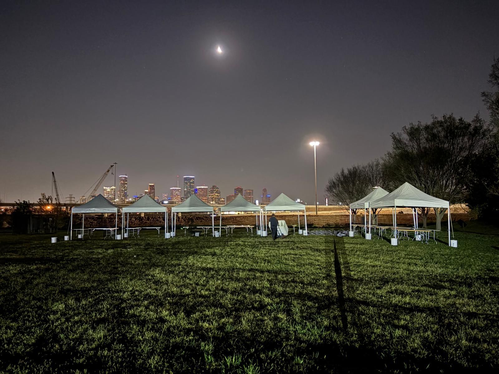 Tented market at night with city skyline background, crescent moon visible.