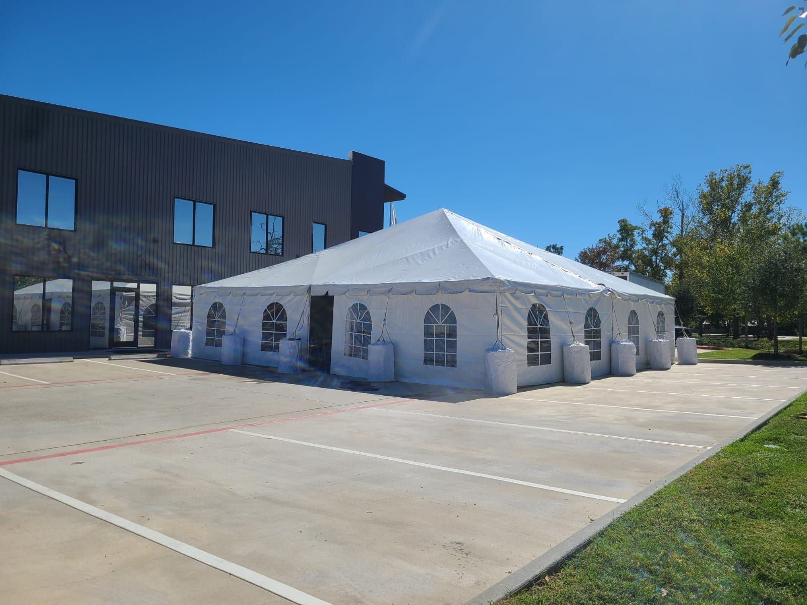 White tent set up on concrete next to a dark building on a sunny day.