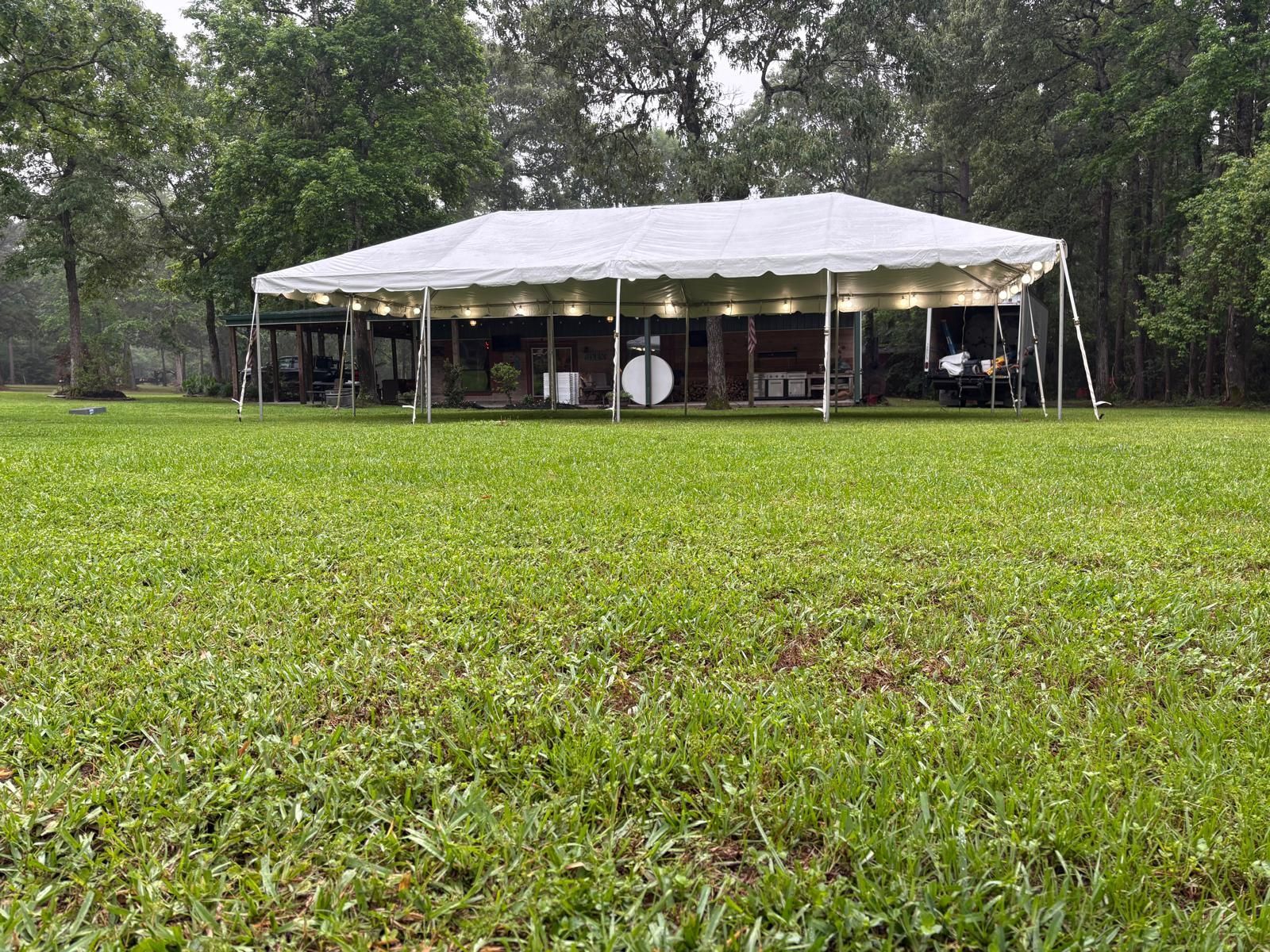 White tent set up in a grassy yard, surrounded by trees. It's a cloudy day.