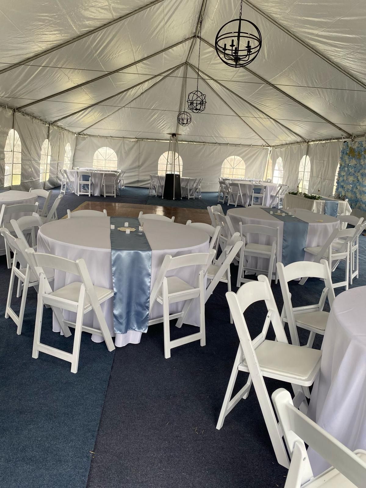 White chairs and tables set up inside a large tent for an event.