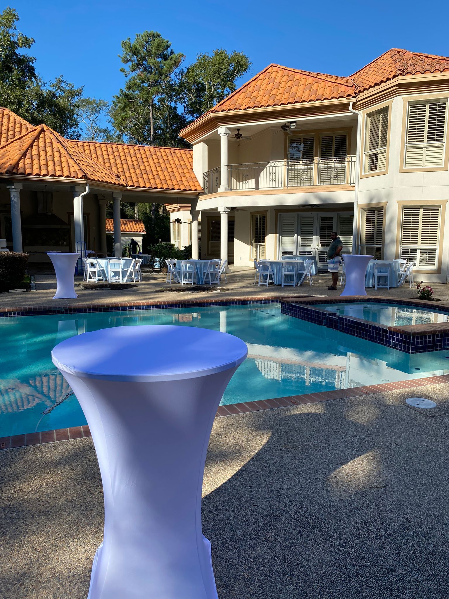 Poolside event with tables and chairs set up near a large house with terracotta roof.