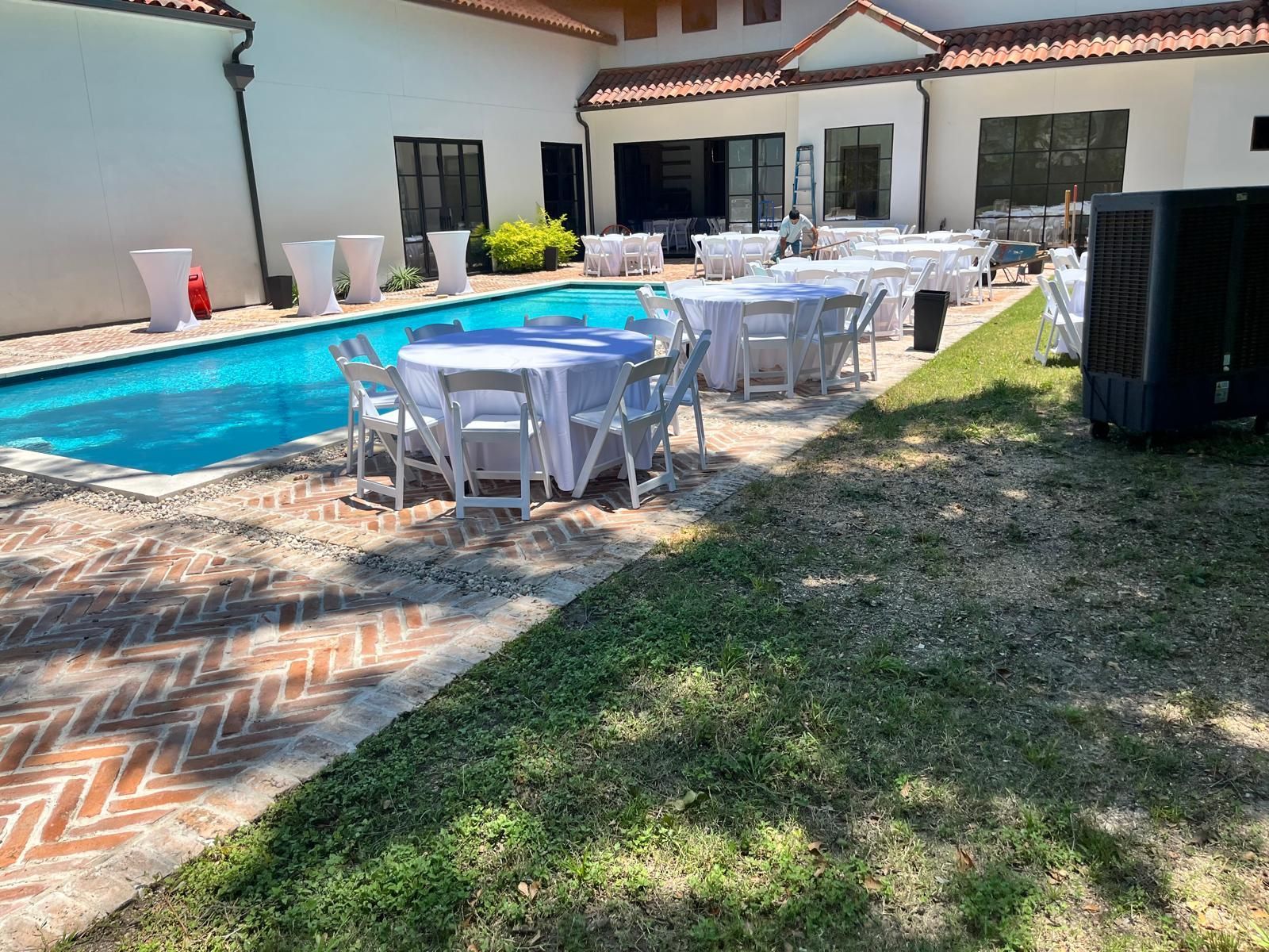 Outdoor event space with tables, chairs, and a pool; a building with white walls and a red tile roof.