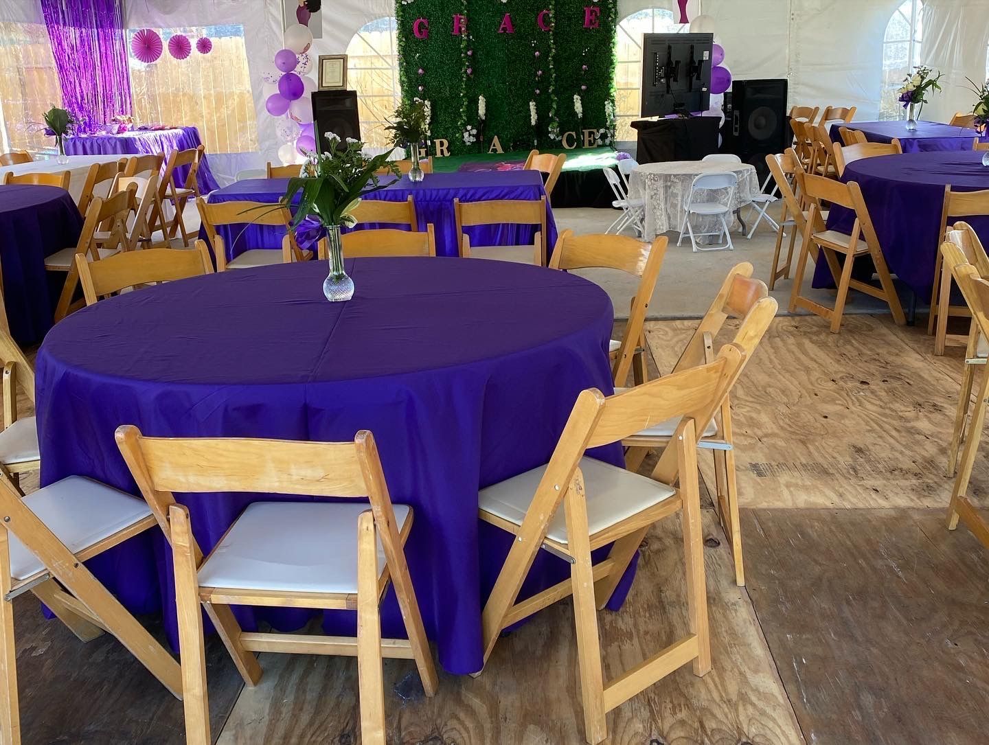 Tables set for an event inside a tent with purple tablecloths and wooden chairs.