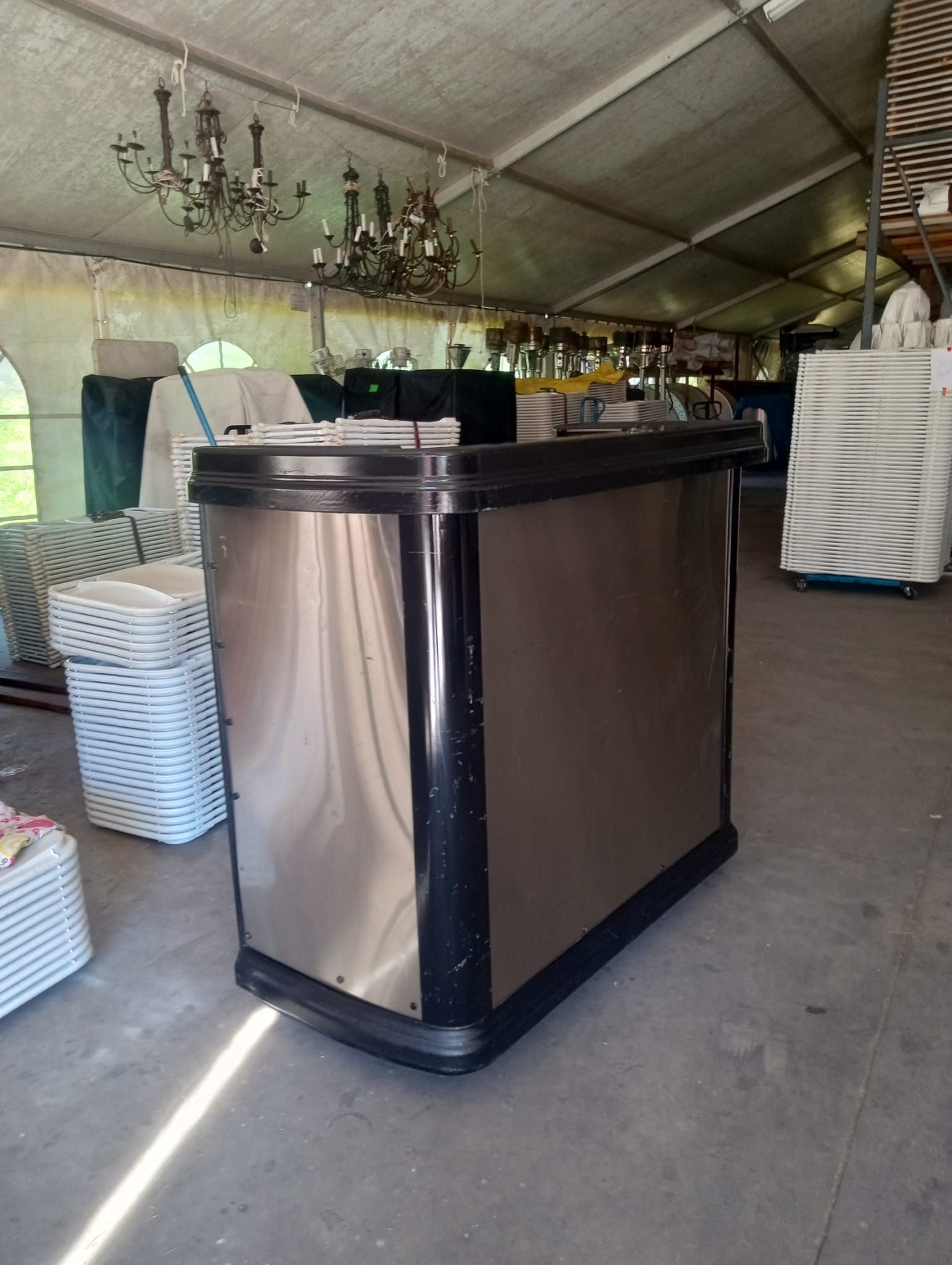 A silver bar with black trim is set up inside a tent, with stacks of chairs nearby.