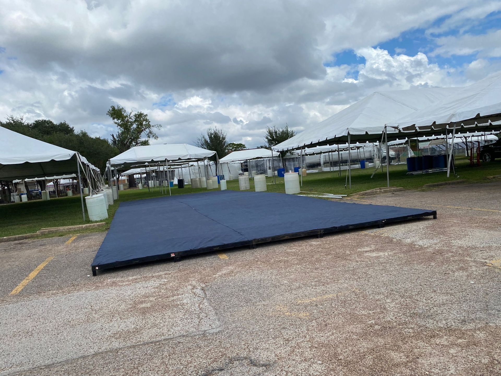 Blue dance floor set up in gravel parking lot, with white tents and cloudy sky in the background.
