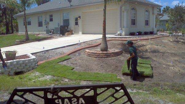 Person laying sod in front yard of a beige house.
