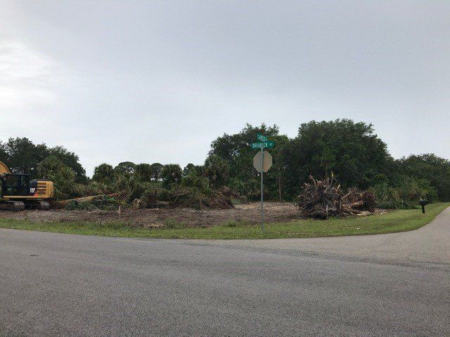 Construction site at a road intersection. Land cleared of trees, a yellow excavator, street sign, cloudy sky.