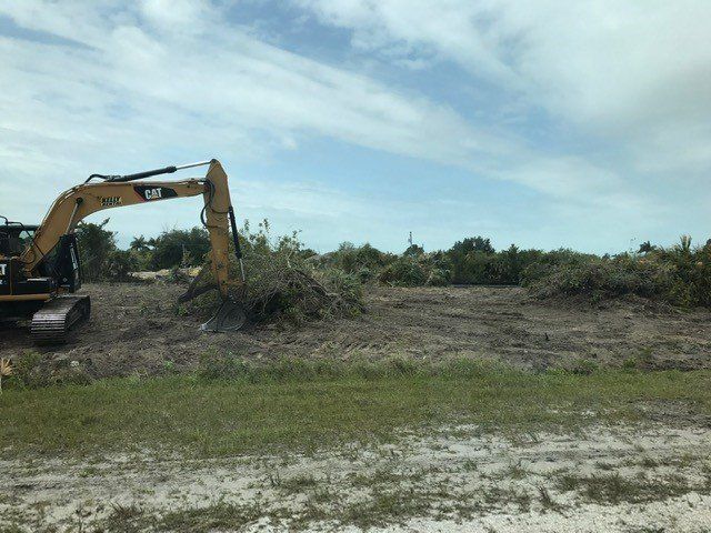 Excavator clearing brush in an open field under a partly cloudy sky.