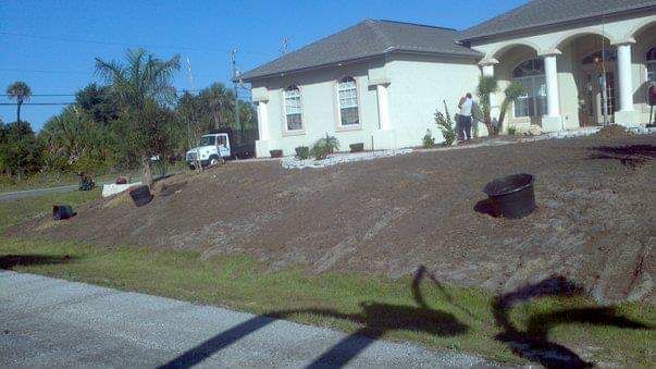 House with sloped yard, truck, and person standing. Dark mulch, and green grass are visible.