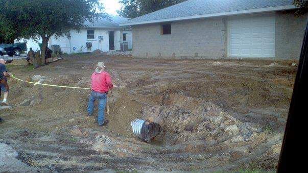 Man pulling barrel from dirt pile near a house and garage; yellow tape present.