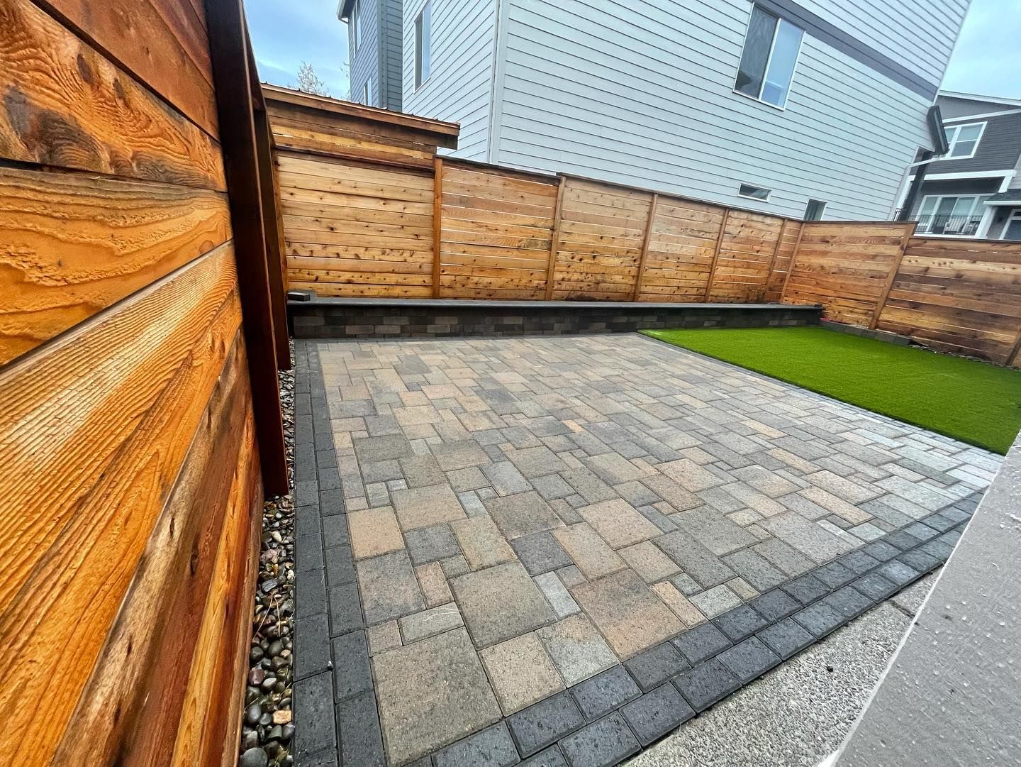 A brick patio with a wooden fence in the backyard of a house.