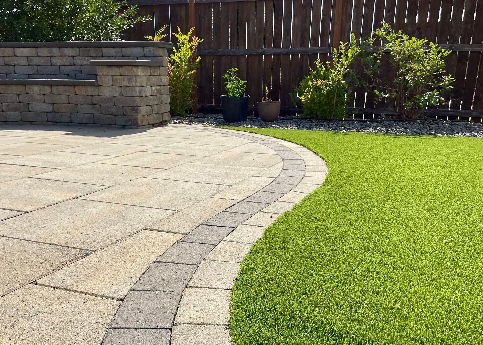 A patio with a wooden fence in the background and a lush green lawn.