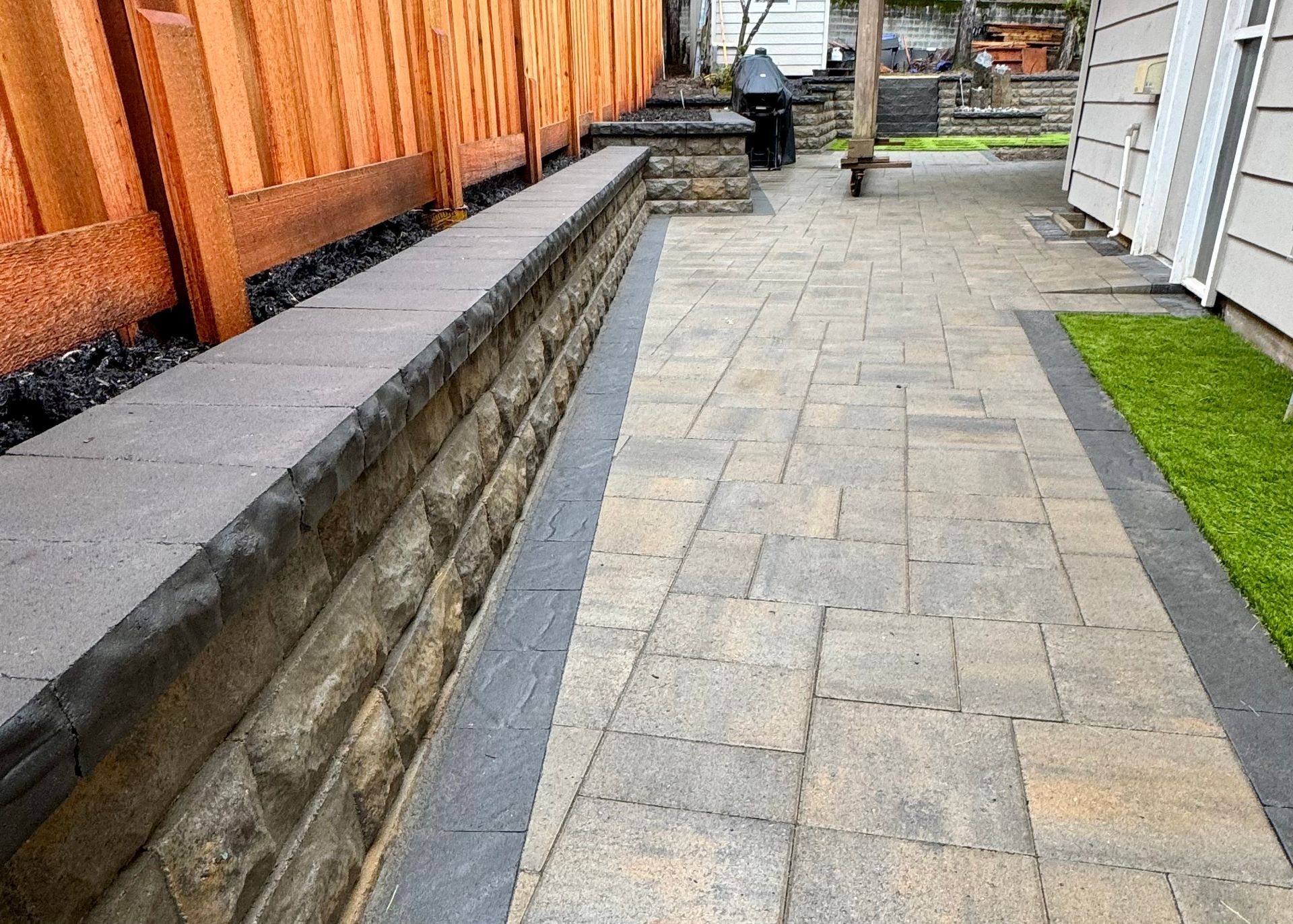A brick walkway leading to a house with a wooden fence.