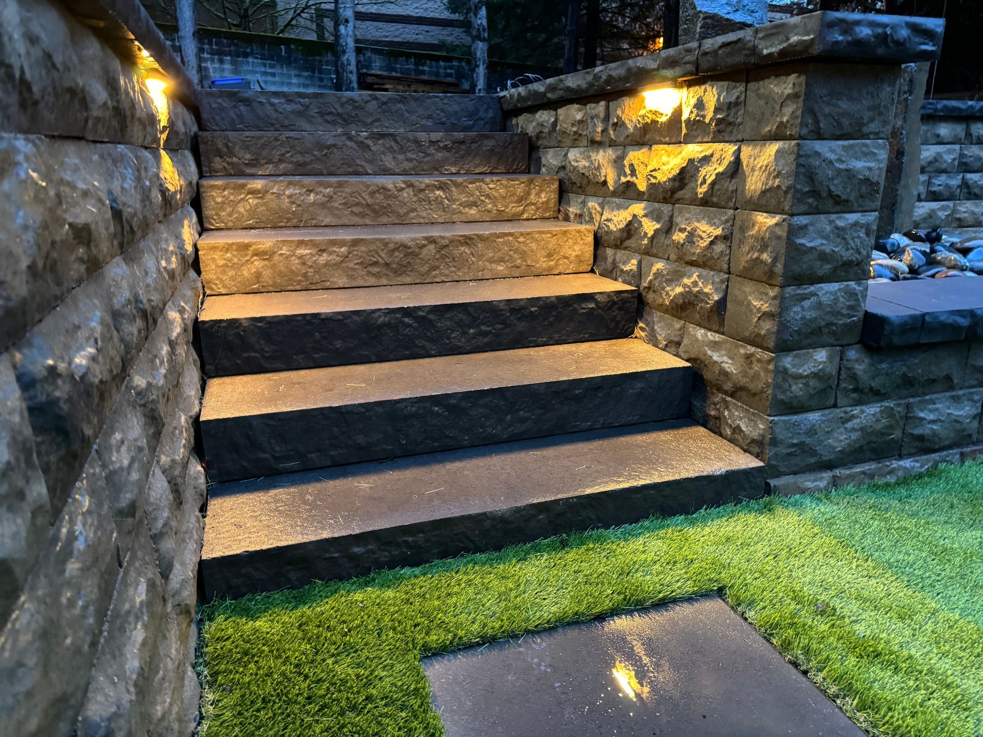 A set of stairs leading up to a stone wall with lights on them.