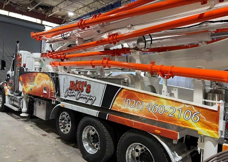 Concrete pumping truck with orange boom arm extended; white, orange, and black color scheme. Company logo 