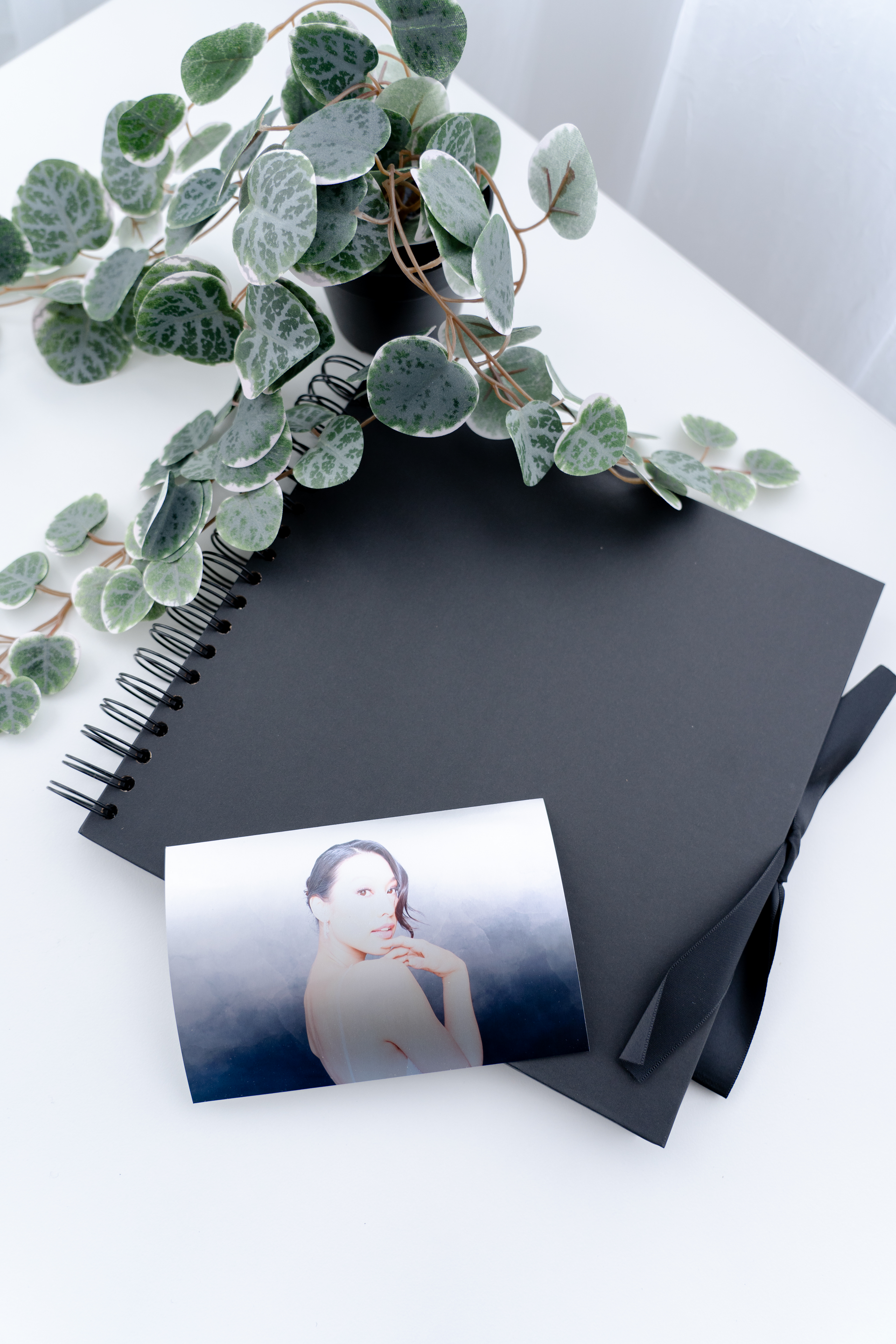 A black notebook with a picture of a woman on it is sitting on a table next to a plant.