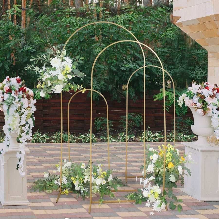 A gold arch surrounded by vases of flowers on a brick sidewalk.