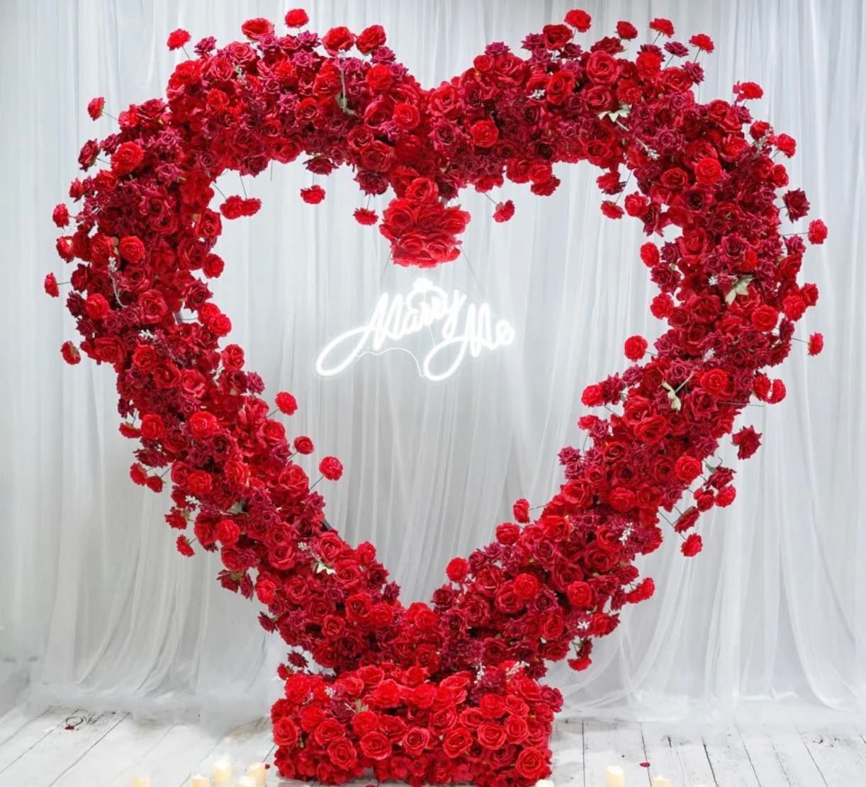 A heart made of red roses with a neon sign that says marry me