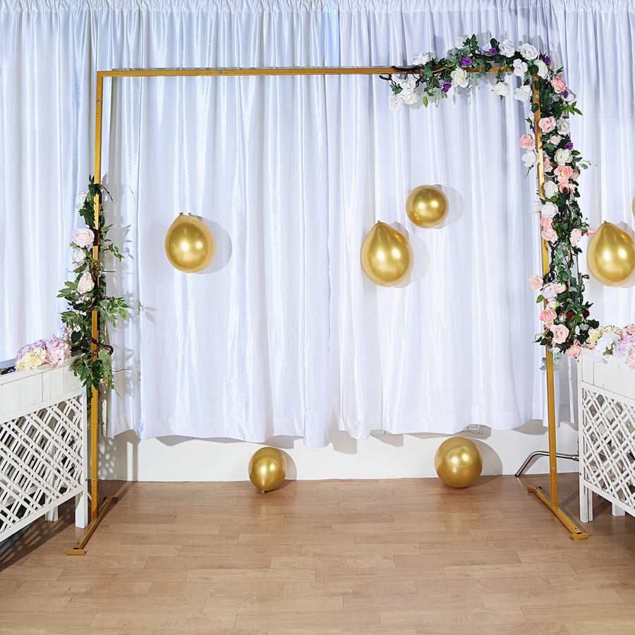 There is a gold arch with balloons and flowers in front of a white curtain.
