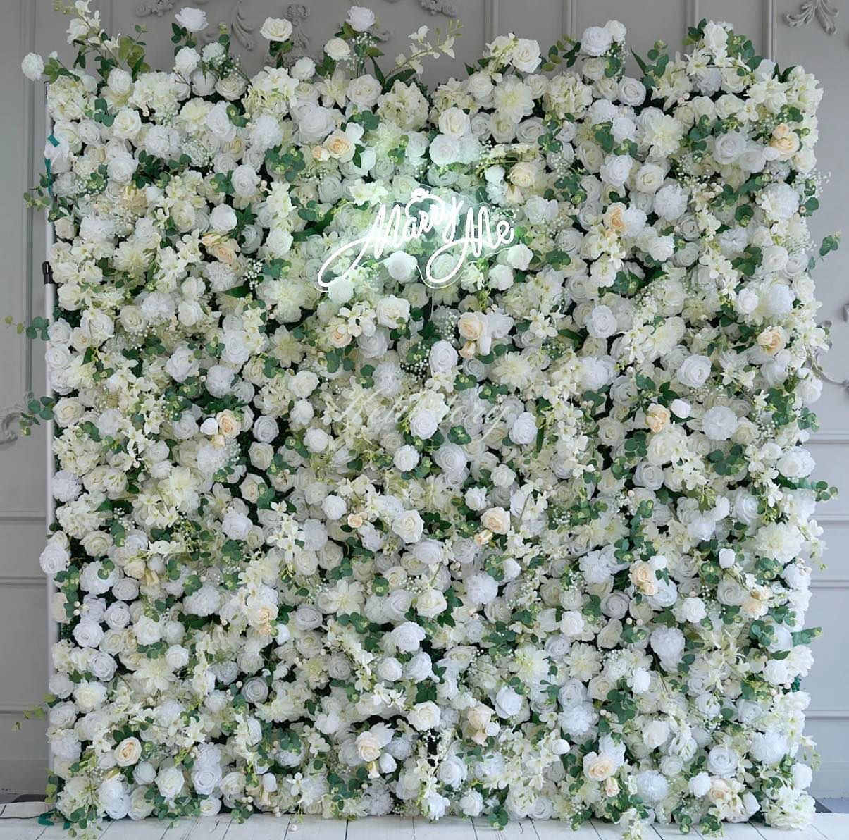 A wall covered in white flowers and greenery with a neon sign.