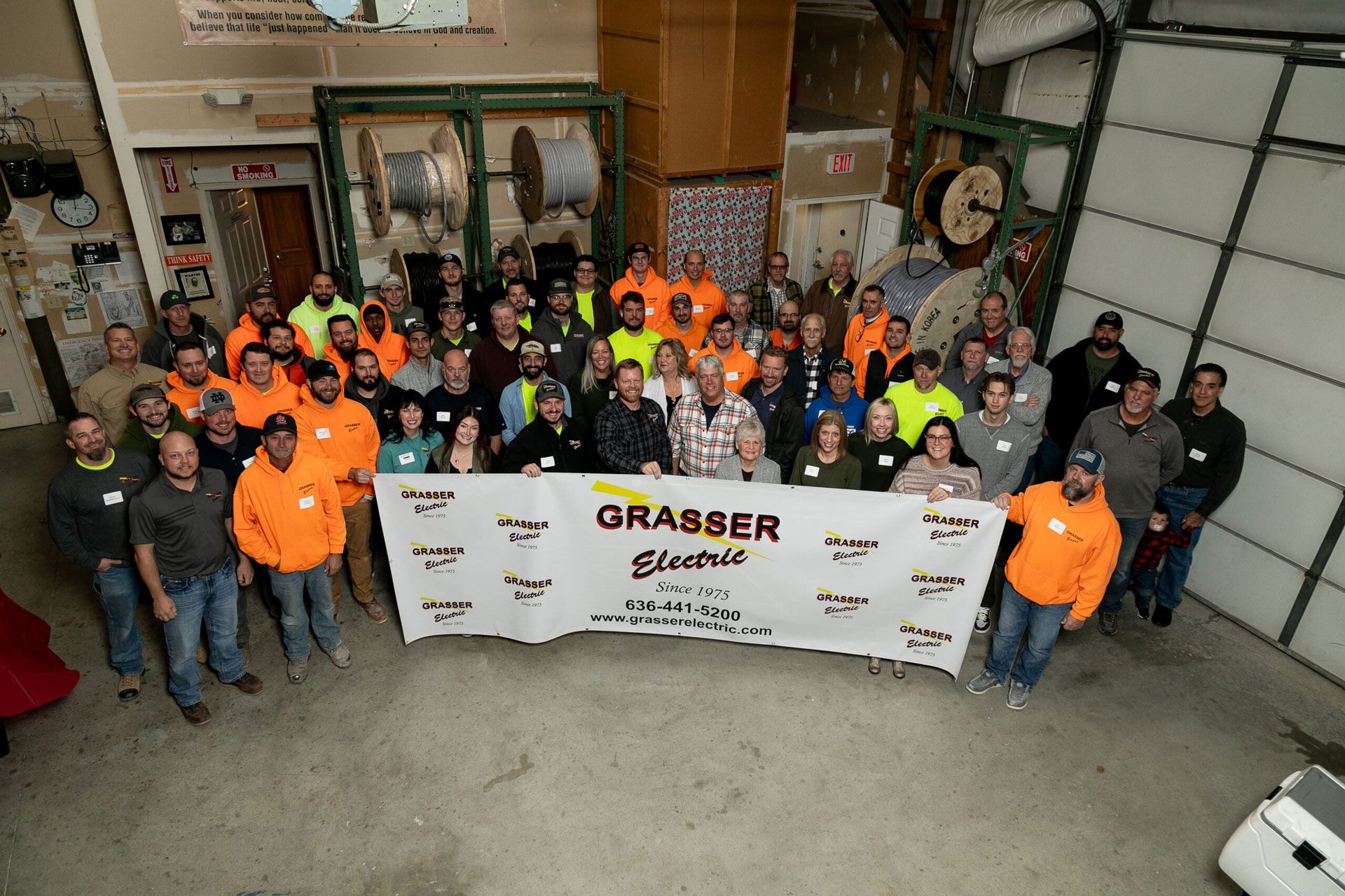 Group of workers in orange and gray safety gear holding a “GRABBER” banner in a warehouse garage