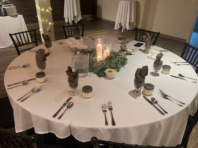 Round banquet table set with white linens, candles, folded napkins, and place settings in a dim event room
