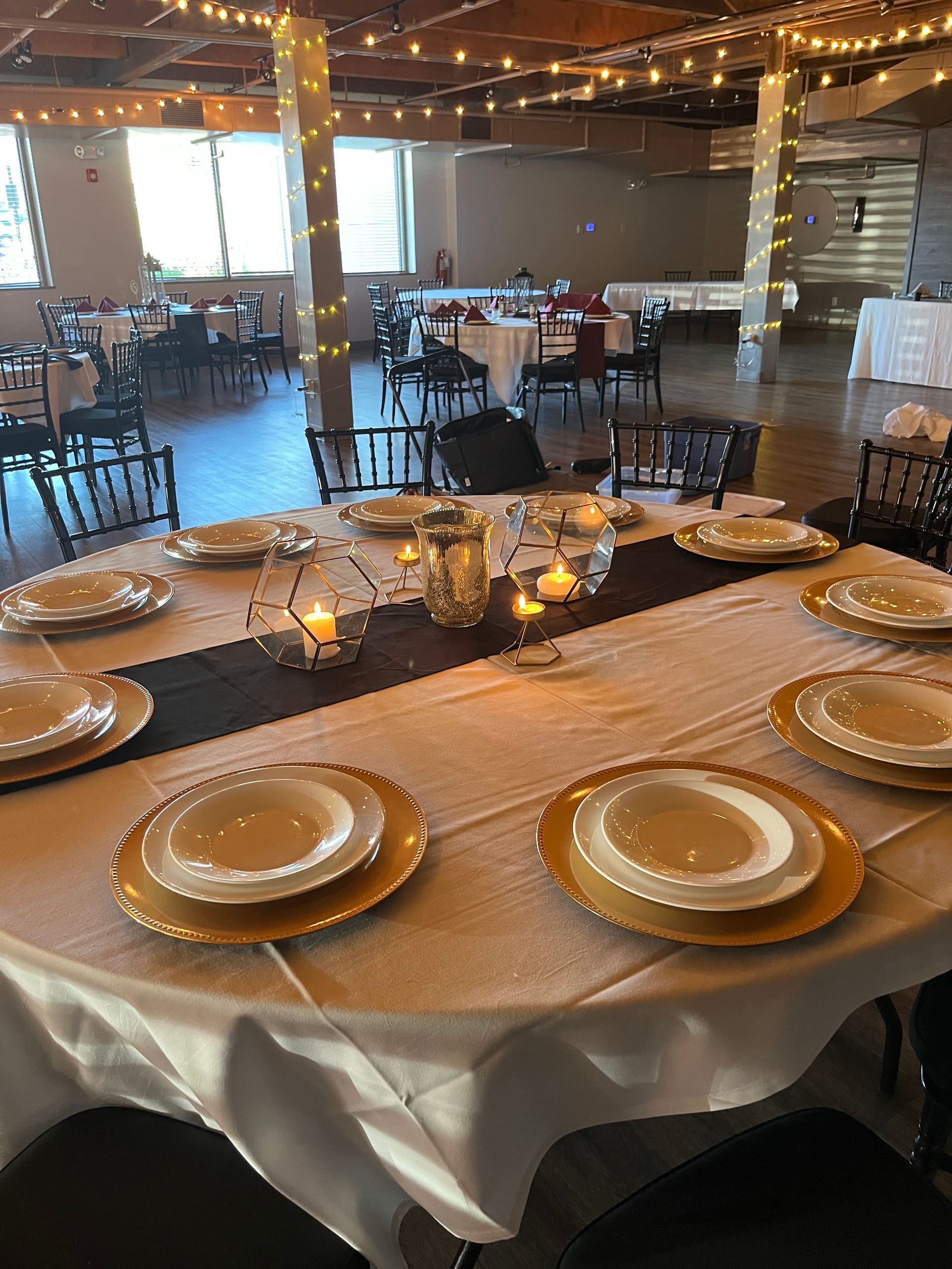 Round banquet table set with white and gold plates, candles, and chairs in a warmly lit event hall