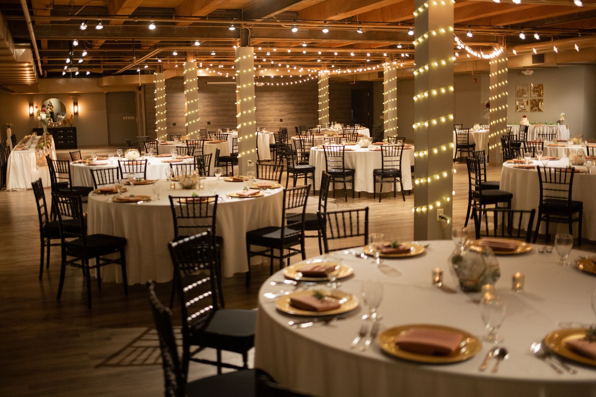Elegant banquet hall with round tables, white tablecloths, and warm string lights overhead