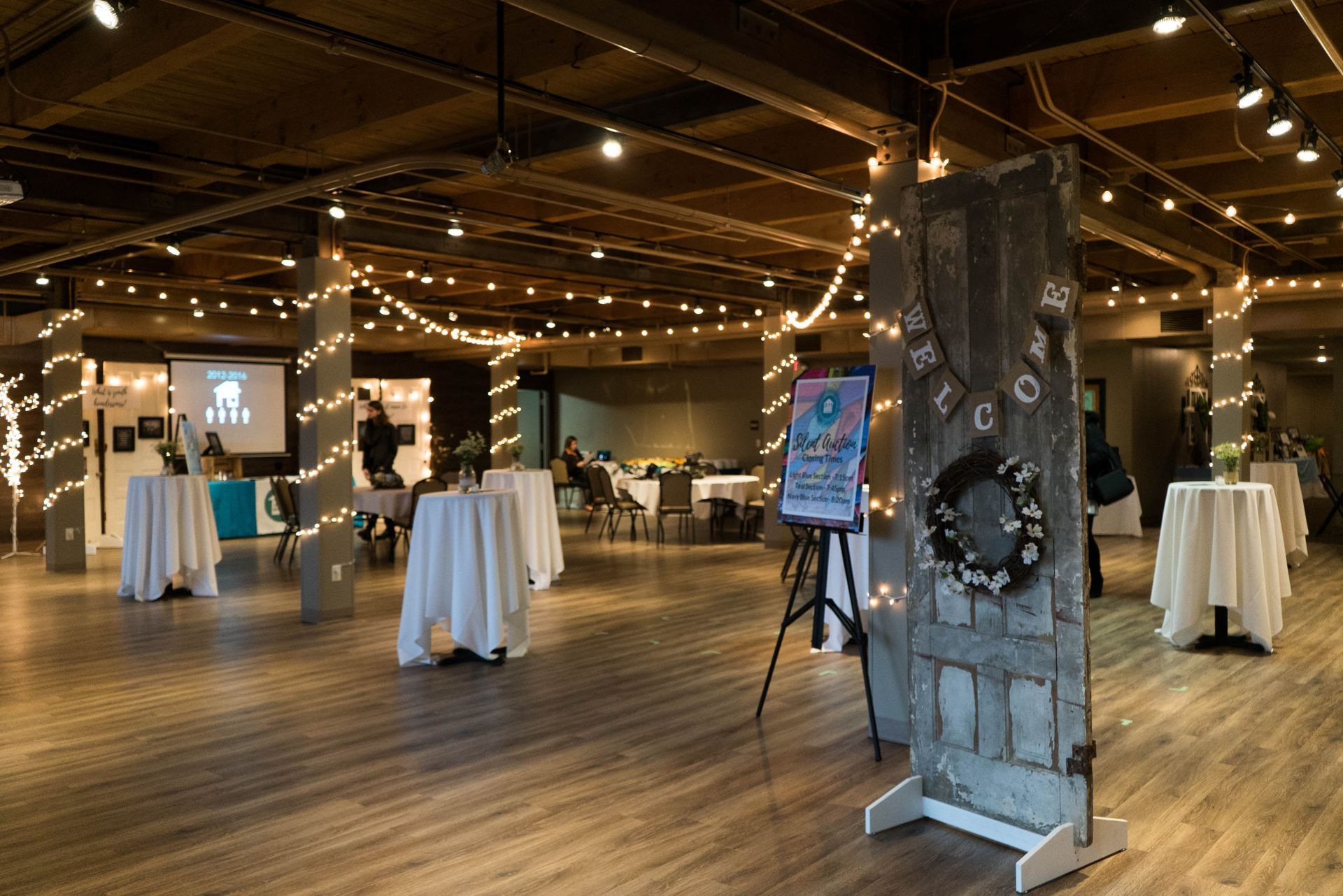 Indoor event space with string lights, cocktail tables, and a rustic wooden pillar display