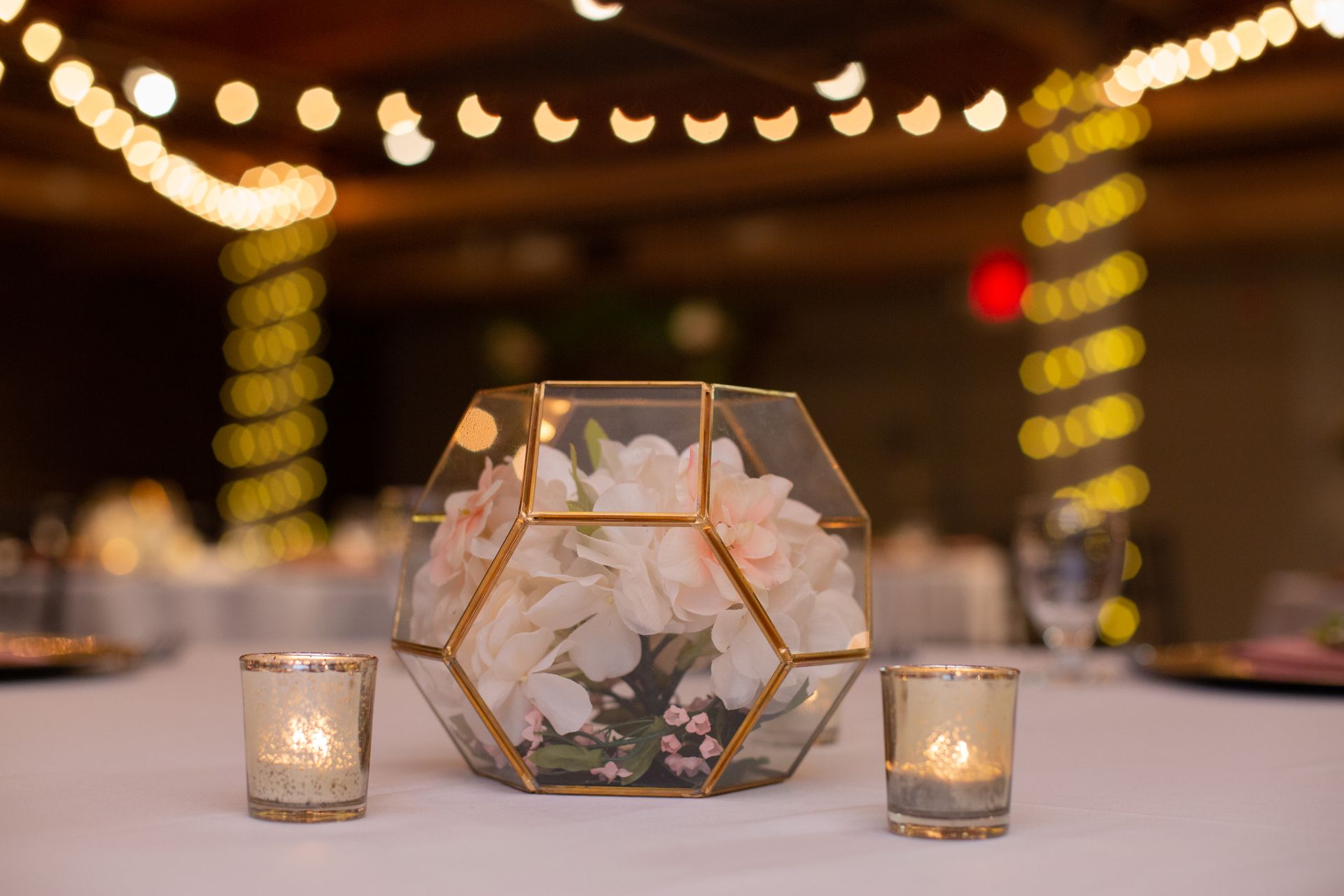 Geometric glass terrarium centerpiece with white flowers and lit candles on a softly lit table